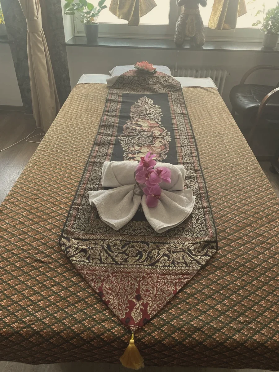 Massageliege mit goldenem Brokatläufer und Handtuchschleife